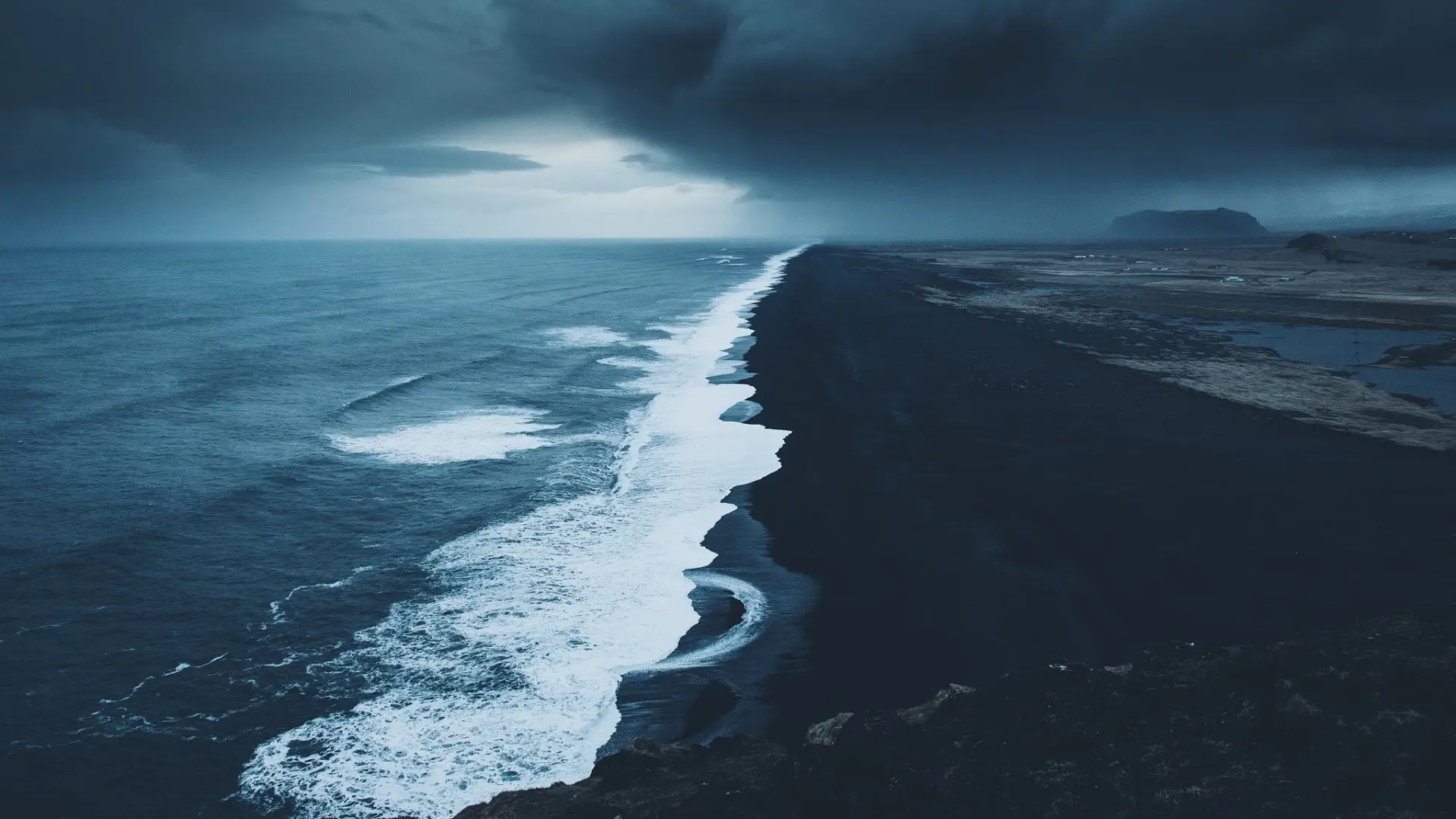 a_black_sand_beach_with_waves_and_clouds_above.jpg