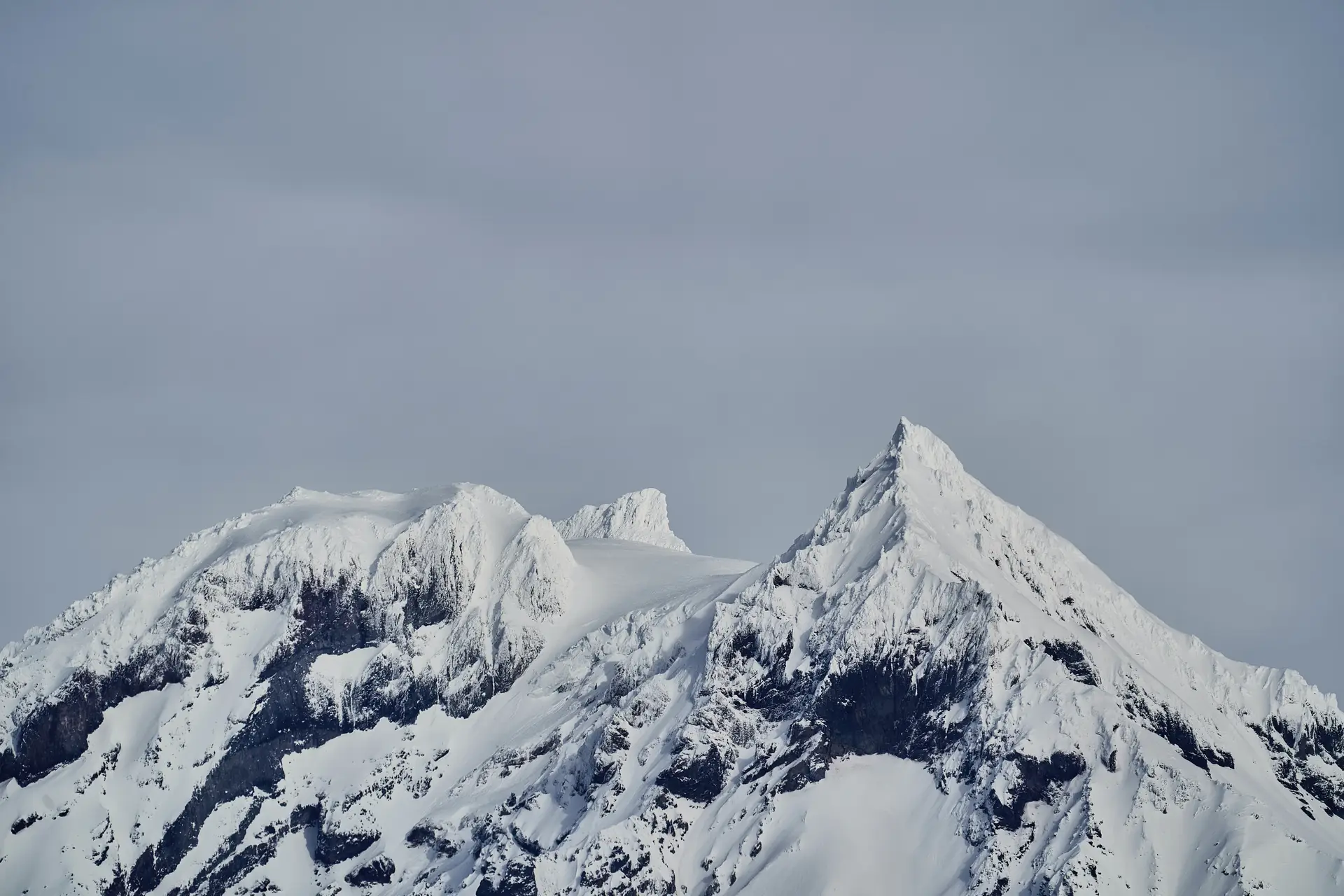 a_snowy_mountain_tops_with_a_grey_sky.jpg